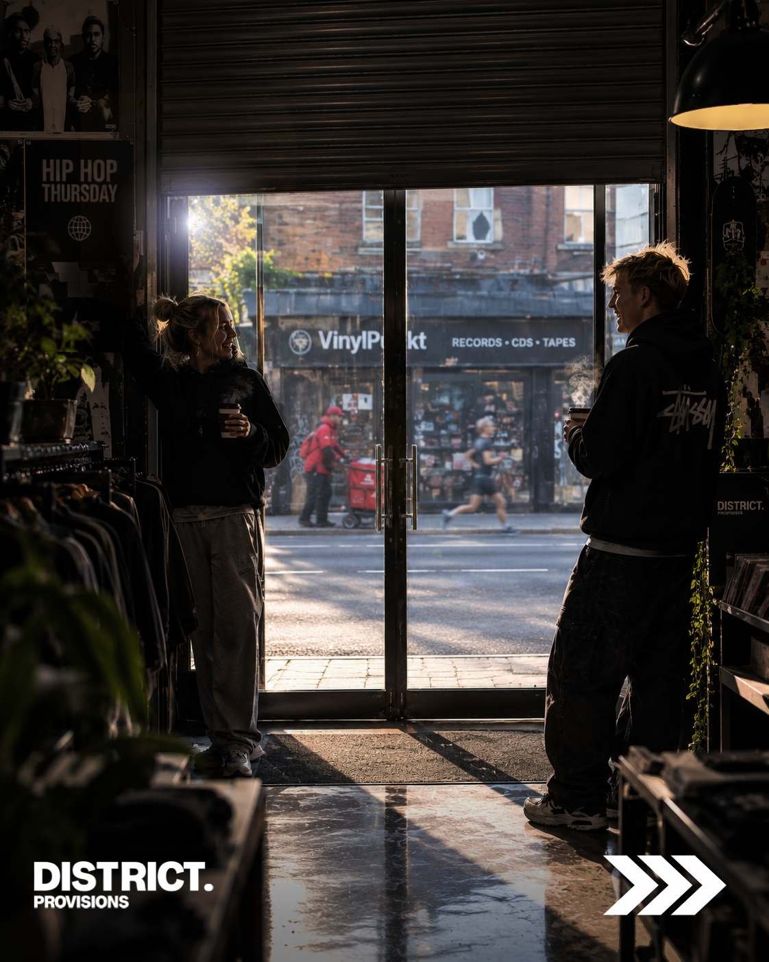 Liberty opens the roller shutter at DISTRICT. PROVISIONS while chatting with Sebz over a takeaway coffee, with the HIP HOP THURSDAYS sign on the wall and VinylPunkt records opening across the road.